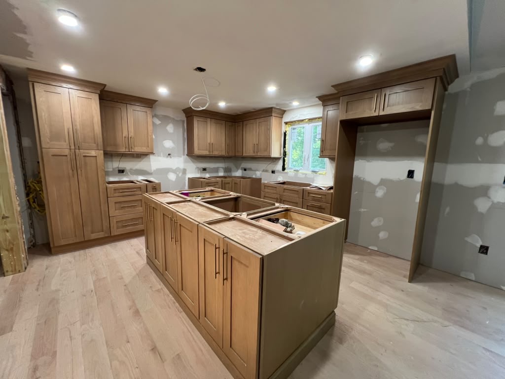 Natural oak shaker cabinetry and a large island set in place during a kitchen installation by Division Seven Millwork