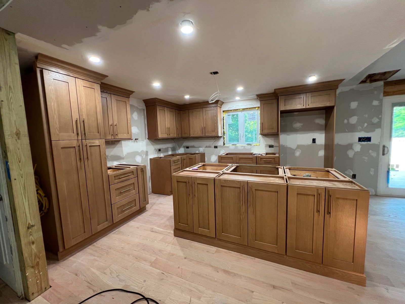 Floor-to-ceiling natural oak pantry cabinets and a framed island during a full kitchen build by Division Seven Millwork