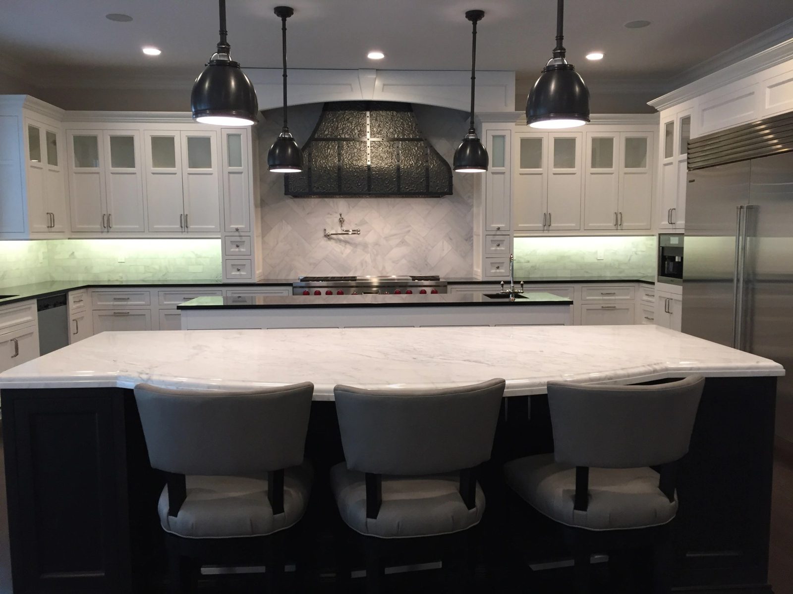 Custom white kitchen with a marble island, herringbone backsplash, and custom range hood built by Division Seven Millwork